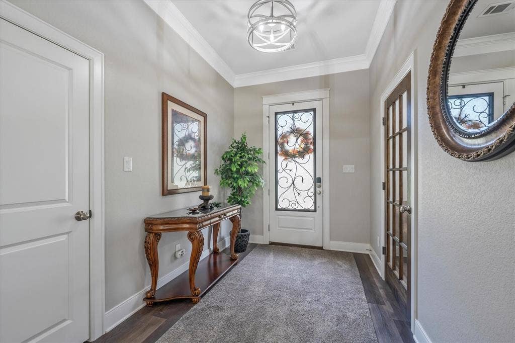14486 Meadow Glen, Lindale, TX 75771 Decorative front door with wrought iron detailing, crown molding, a modern semi-flush mount light fixture, wood-finish flooring, and a paneled interior door