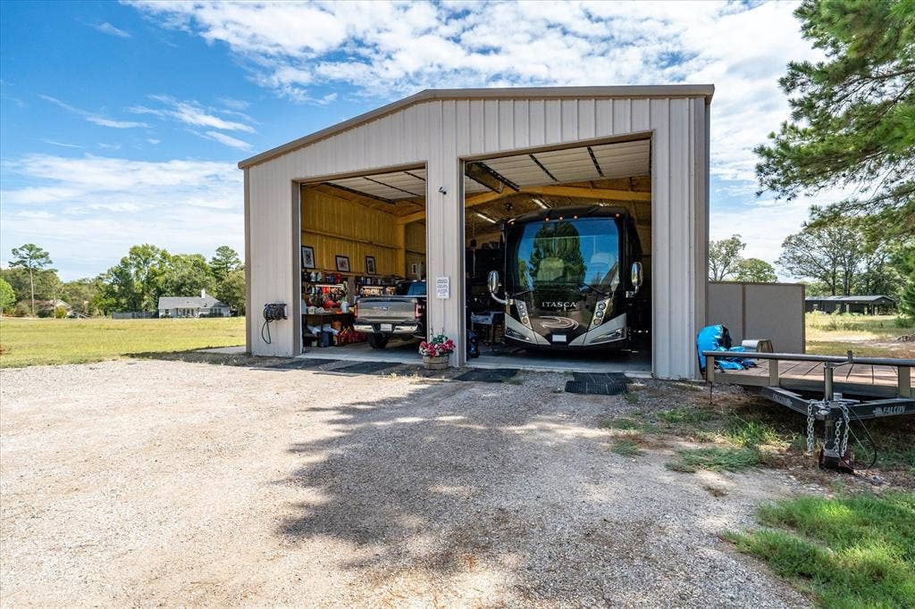 14486 Meadow Glen, Lindale, TX 75771 Two-bay metal structure with roll-up doors, gravel driveway, and a partially visible utility shed