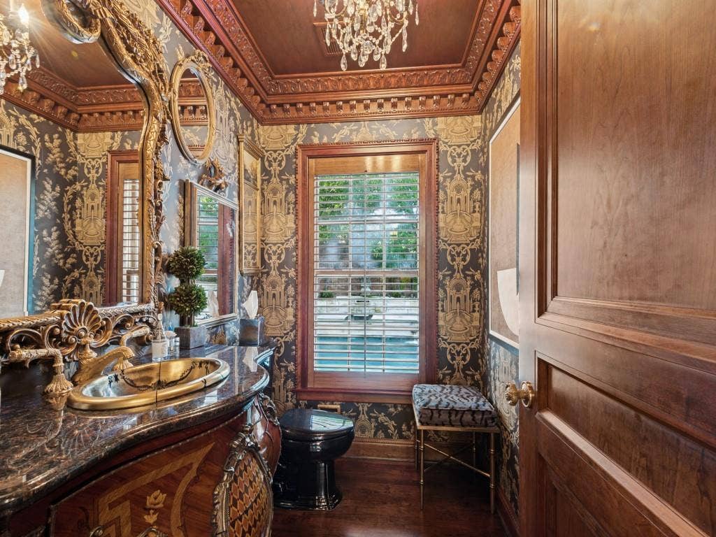 6858 Tokalon Drive, Dallas, TX 75214 Ornate vanity with dark polished stone countertop, decorative metal drop-in sink, intricate wood-paneled door, elaborate crown molding, and custom wood window shutters