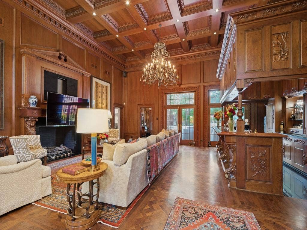 6858 Tokalon Drive, Dallas, TX 75214 Wood-paneled room featuring a coffered ceiling, herringbone hardwood flooring, an ornate built-in bar, a fireplace with carved detailing, and a multi-tiered metal chandelier