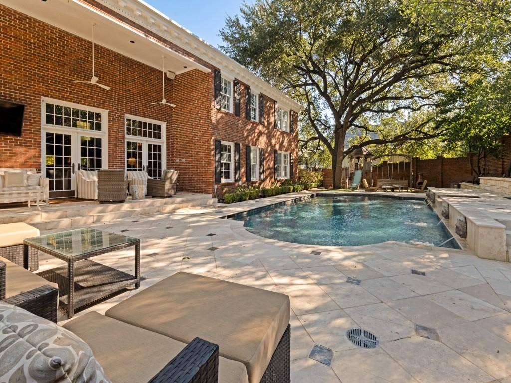 6858 Tokalon Drive, Dallas, TX 75214 Custom brick exterior featuring a covered patio, limestone-paved terrace, inground pool with water features, and mature trees