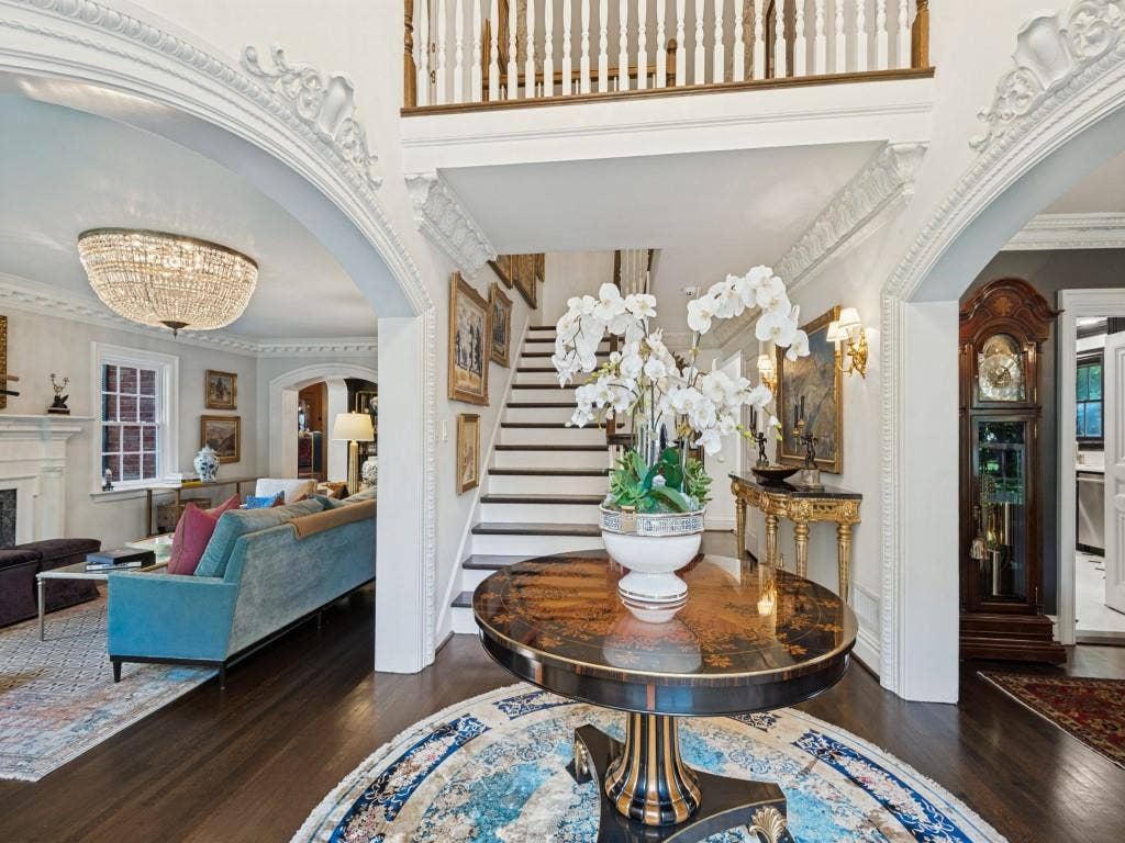 6858 Tokalon Drive, Dallas, TX 75214 Grand foyer featuring intricate crown molding, arched entryways, dark wood-finish flooring, a crystal chandelier, and a staircase with a wooden handrail and balusters