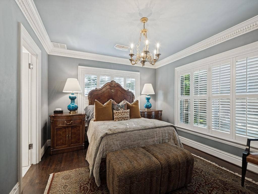 6858 Tokalon Drive, Dallas, TX 75214 Bedroom featuring wood-finish flooring, intricate crown molding, white plantation shutters, and a classic metal chandelier