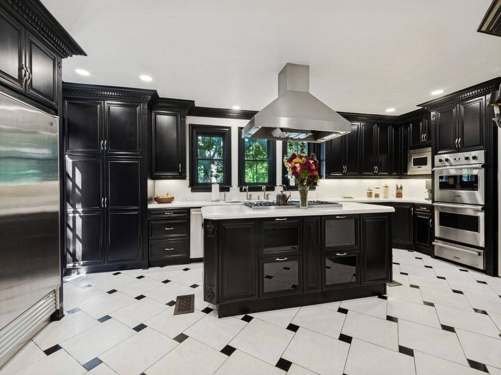 6858 Tokalon Drive, Dallas, TX 75214 Kitchen featuring custom black cabinetry, a central island with a contrasting stone countertop, stainless steel appliances, a stainless steel range hood, and tile flooring with a geometric pattern