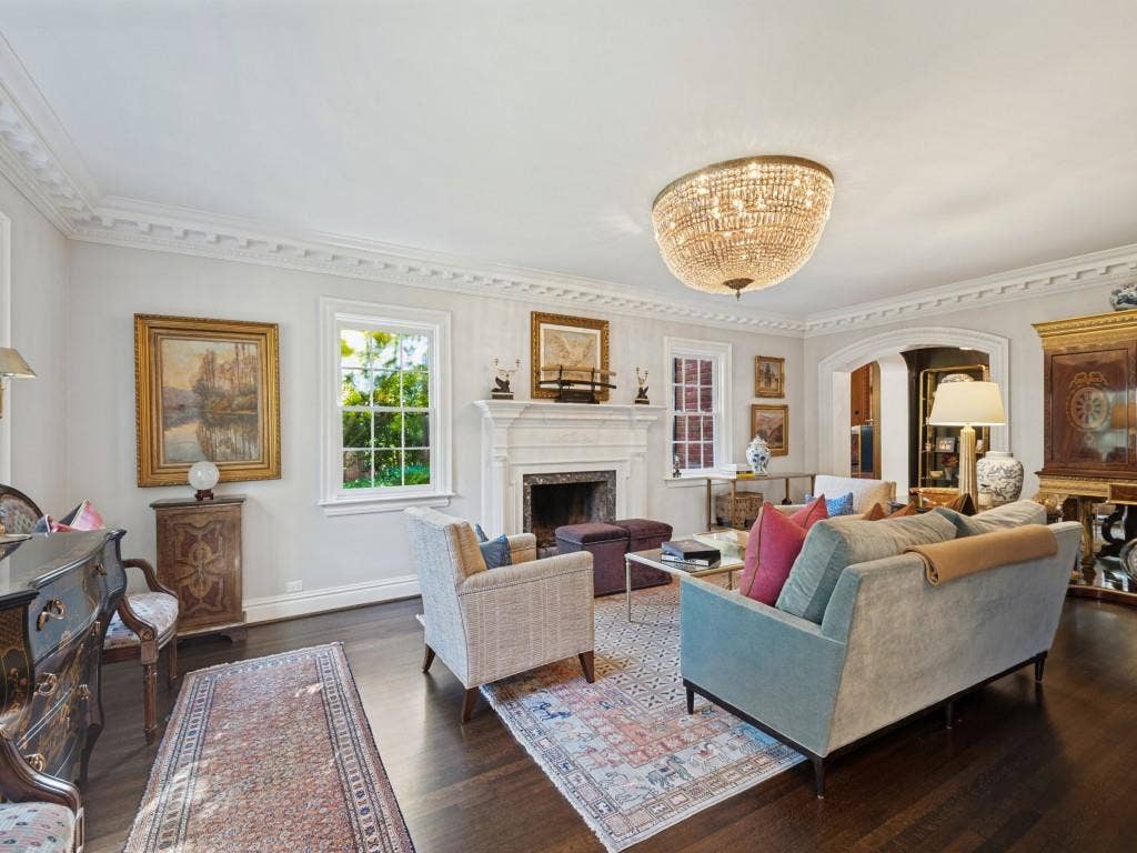6858 Tokalon Drive, Dallas, TX 75214 Living space featuring dark wood-finish flooring, crown molding, a central crystal chandelier, and a masonry fireplace with a white mantel