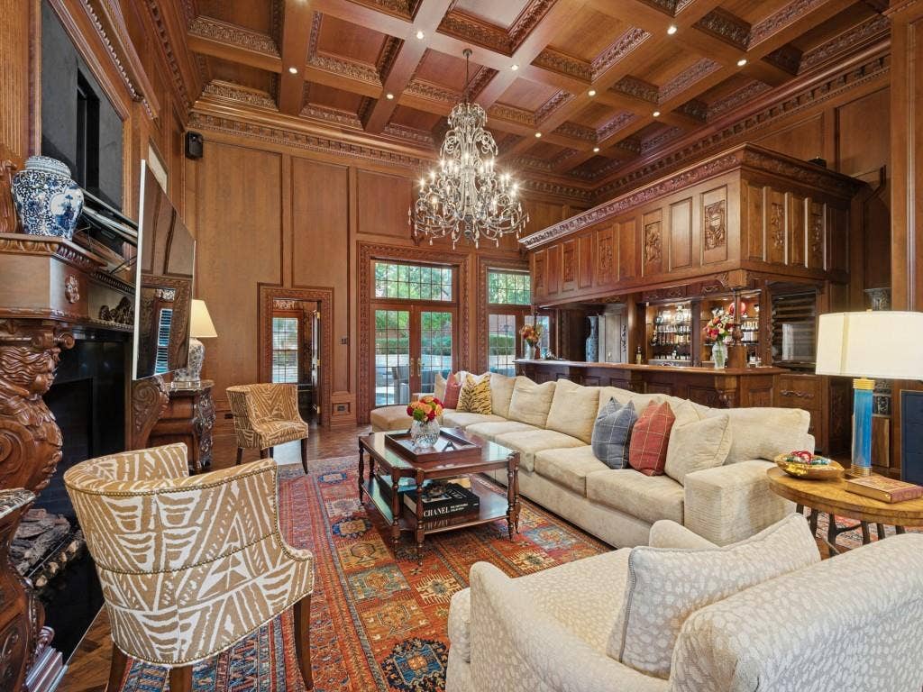 6858 Tokalon Drive, Dallas, TX 75214 Custom wood-paneled walls, coffered ceilings with intricate crown molding, carved wood fireplace surround, full-length built-in bar, and glass-paneled double doors