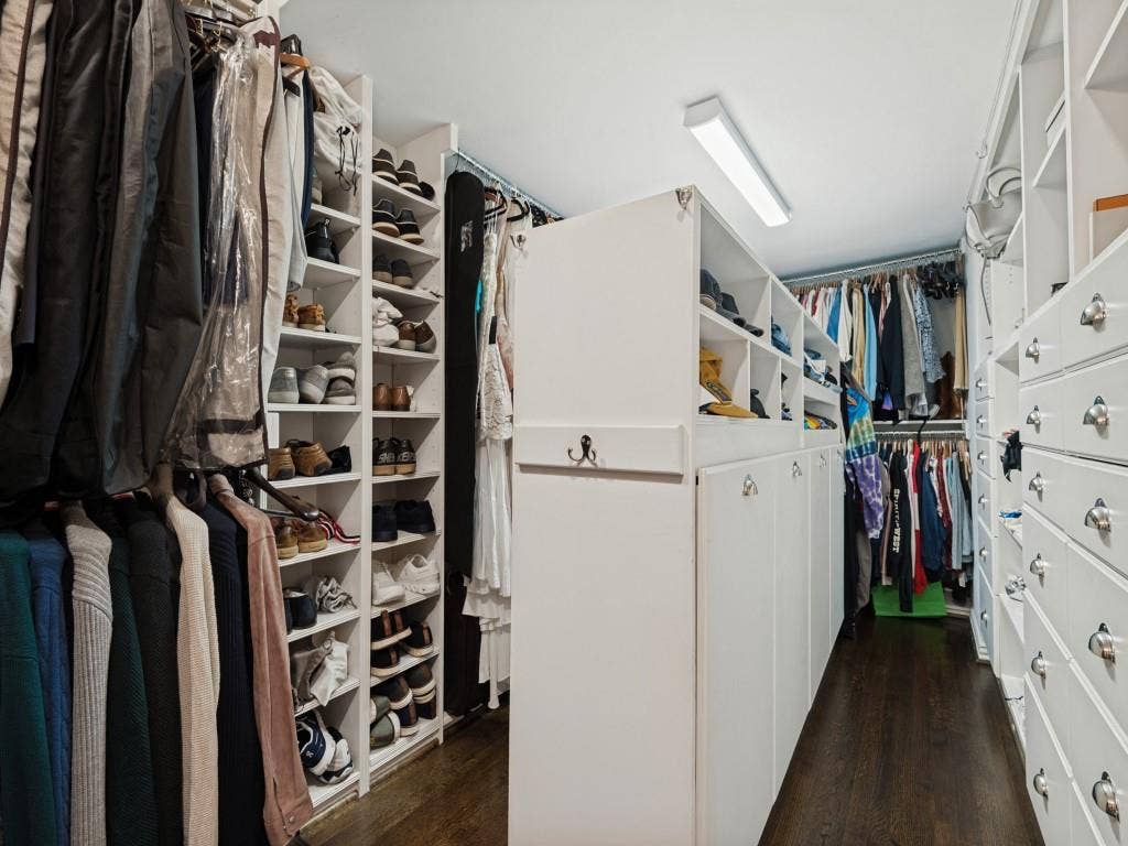 6858 Tokalon Drive, Dallas, TX 75214 Custom walk-in closet featuring extensive white built-in cabinetry, floor-to-ceiling shelving, integrated drawer stacks, and dark wood-finish flooring