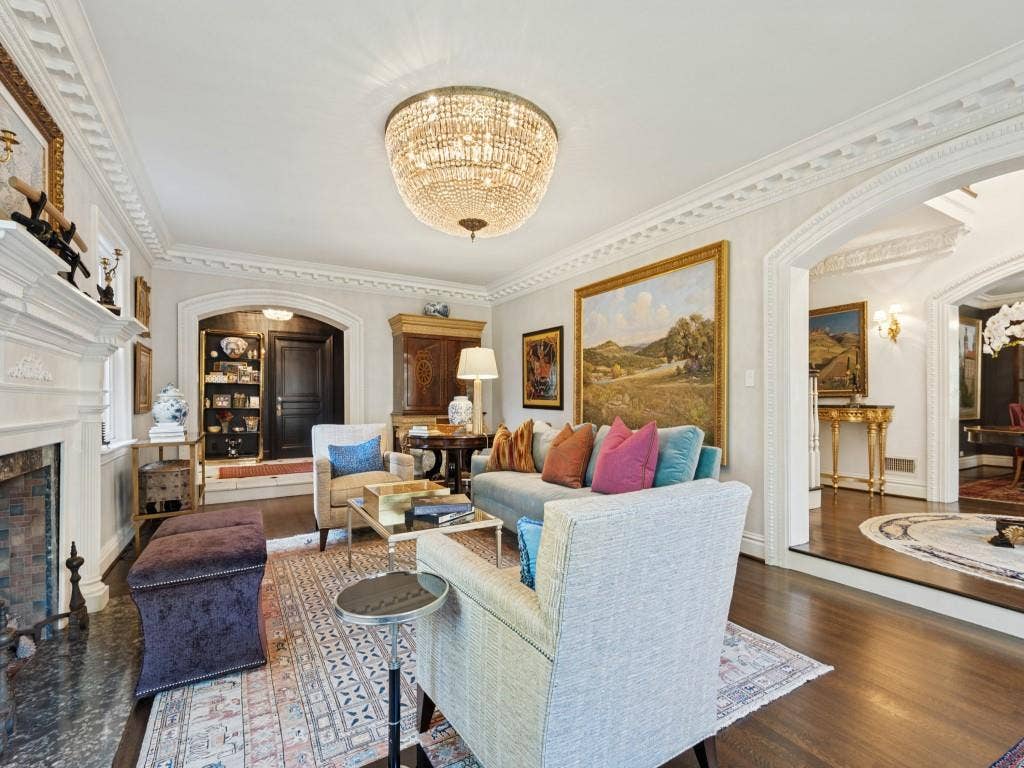 6858 Tokalon Drive, Dallas, TX 75214 Living room featuring ornate crown molding, a central crystal chandelier, a stone-surround fireplace, arched entryways, and wood-finish flooring