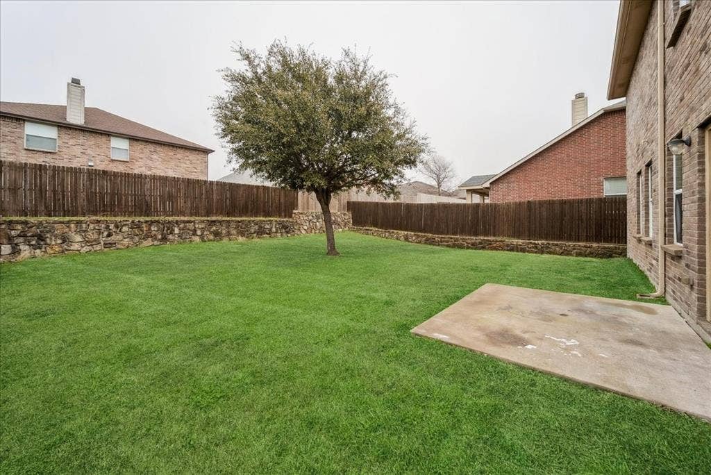 Expansive green lawn with a mature tree, concrete patio, and stone retaining wall