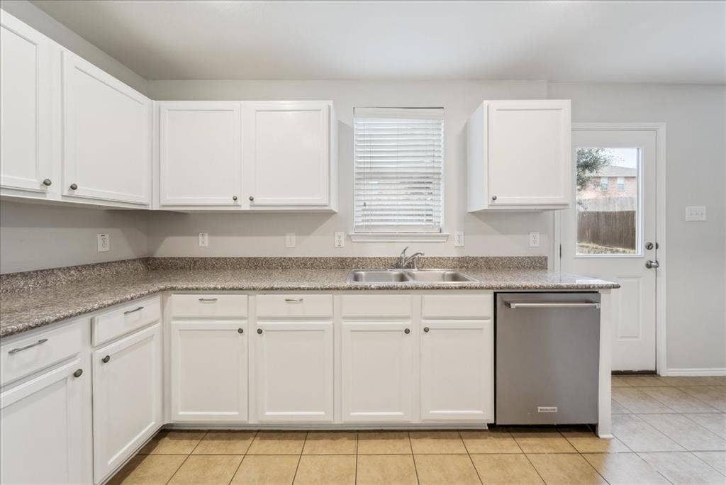 Kitchen featuring white shaker-style cabinetry, a stainless steel double basin sink, stone-look countertops, and a tile flooring