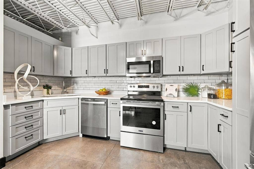 219 S 4th Street, #608, Waco, TX 76701 Kitchen featuring contemporary grey cabinetry, stainless steel appliances, white subway tile backsplash, and light-toned countertops