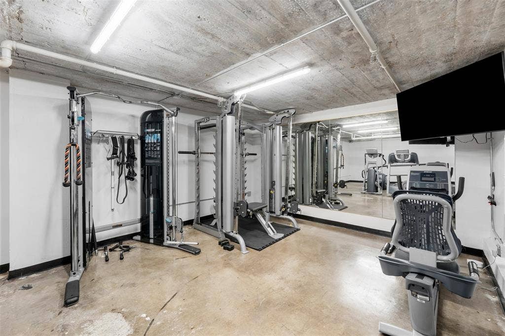 219 S 4th Street, #608, Waco, TX 76701 Dedicated fitness space featuring exposed concrete ceiling, industrial fluorescent lighting, polished concrete flooring, large wall-mounted mirror, and a wall-mounted display