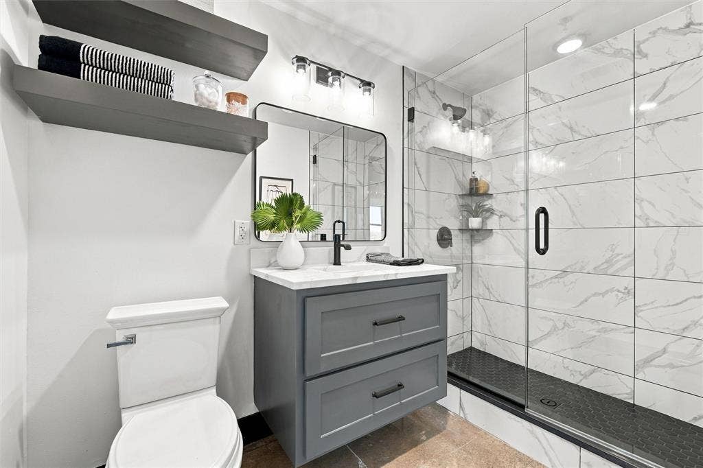 219 S 4th Street, #608, Waco, TX 76701 Modern bathroom featuring a single vanity with a white countertop, framed mirror, and a glass-enclosed shower with white tiled walls and a dark hexagonal floor