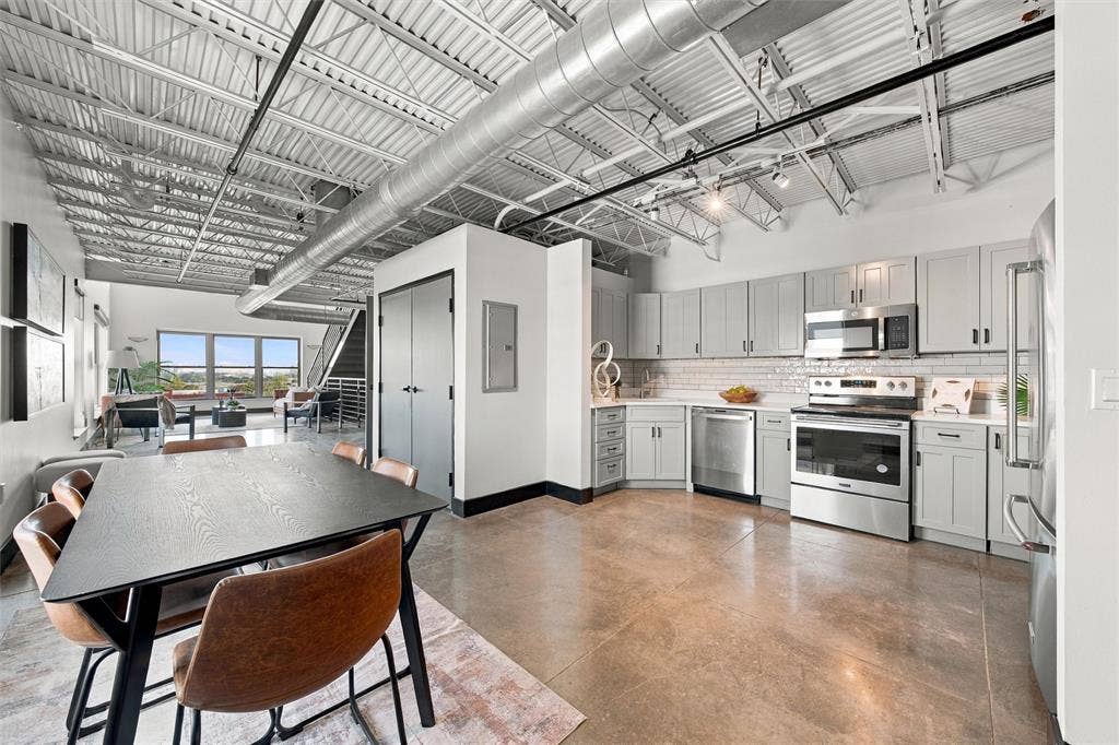 219 S 4th Street, #608, Waco, TX 76701 Open-concept living space featuring exposed ceiling joists, polished concrete flooring, a full kitchen with stainless steel appliances, and large windows