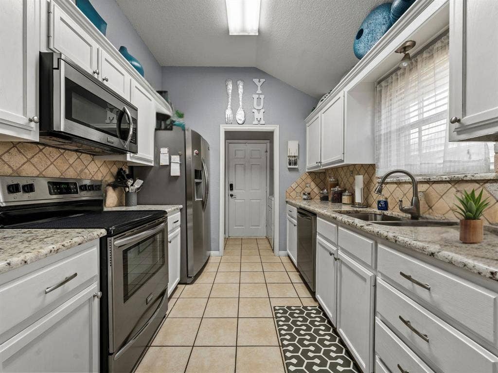 3012 Pinto Loop, Robinson, TX 76706 Galley kitchen featuring white cabinetry, granite countertops, stainless steel appliances, a tile backsplash, and tile flooring