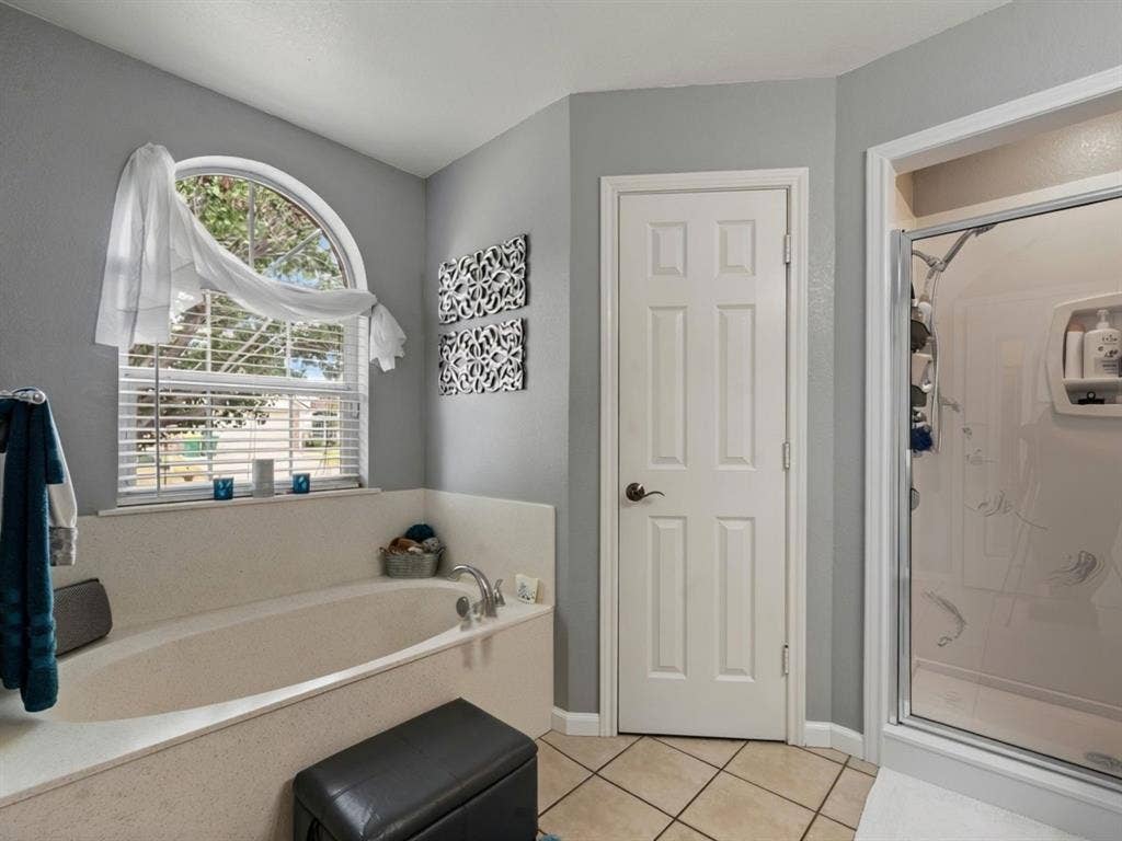 3012 Pinto Loop, Robinson, TX 76706 Garden tub with deck surround, arched window, privacy blinds, tiled flooring, and a stand-up shower enclosure