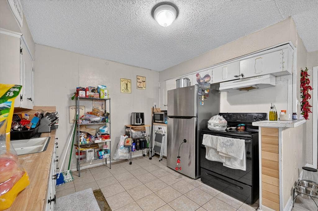 3320 Shorewood Drive, Mesquite, TX 75150 Kitchen featuring durable tile flooring, white cabinetry, wood-finish countertops, stainless steel refrigerator, and a black range