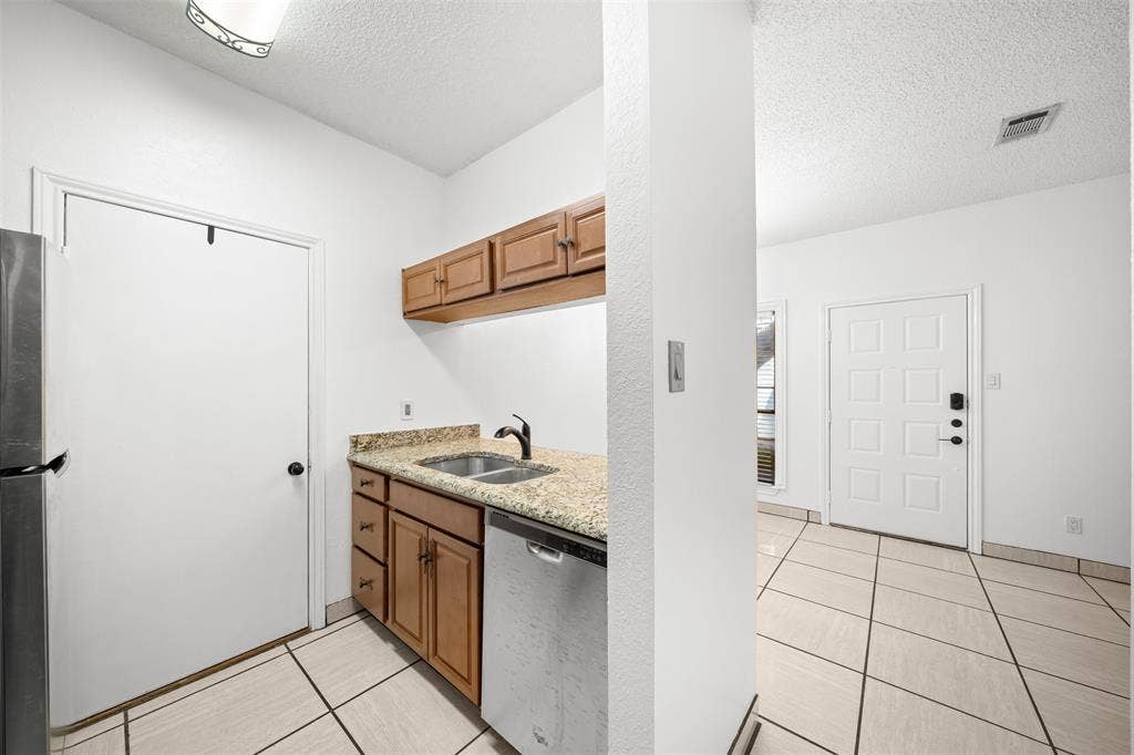 7340 Skillman Street, #909, Dallas, TX 75231 Kitchenette featuring wood cabinetry, stone-finish countertops, stainless steel sink, and integrated dishwasher