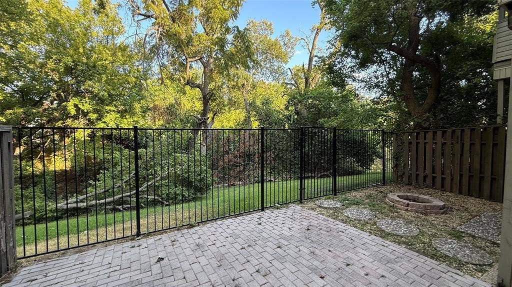 7340 Skillman Street, #909, Dallas, TX 75231 Outdoor patio featuring paver stones, a black metal fence, a wood fence, a fire pit, and stone pavers