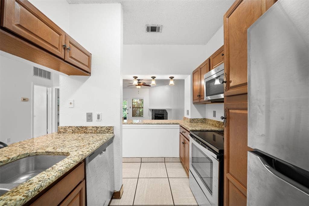7340 Skillman Street, #909, Dallas, TX 75231 Kitchen featuring wood cabinetry, stainless steel appliances, granite countertops, and tiled flooring