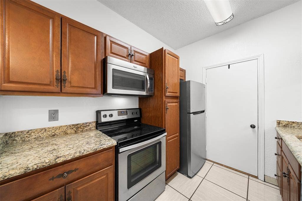7340 Skillman Street, #909, Dallas, TX 75231 Kitchen featuring wood cabinetry, stainless steel appliances, speckled countertops, and tile flooring