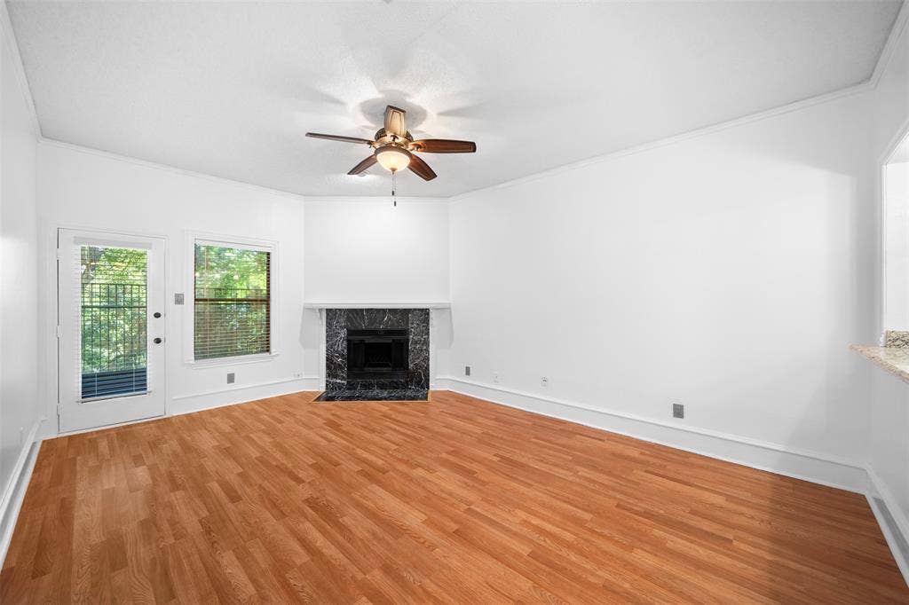 7340 Skillman Street, #909, Dallas, TX 75231 Wood-finish flooring, corner fireplace with a dark stone surround, white walls, and a ceiling fan
