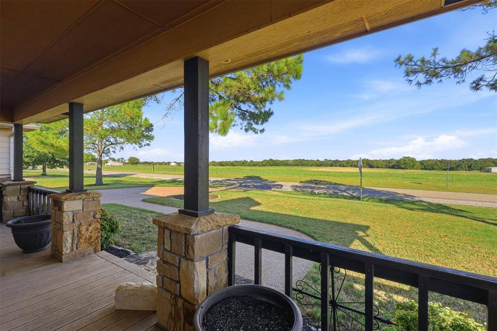 Covered porch with wood-finish decking, stone-clad pillars, and wrought iron railing