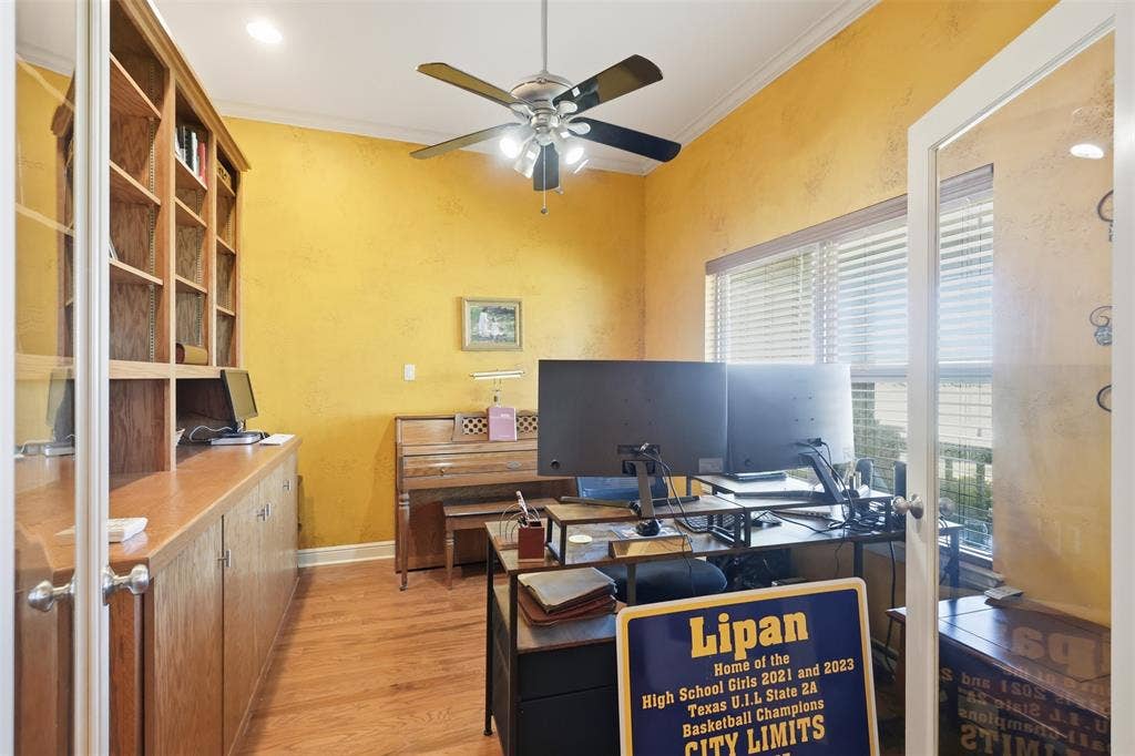 Wood-finish flooring, built-in shelving, glass-panel French doors, ceiling fan with integrated lighting, and crown molding