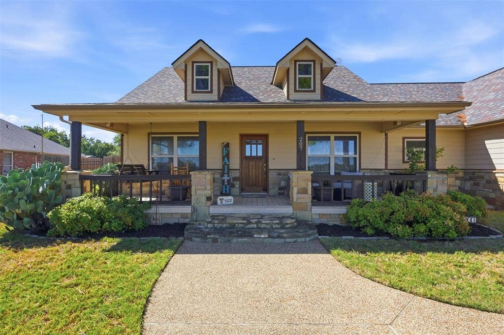 Front exterior with a covered porch, dormer windows, and a stone-clad foundation