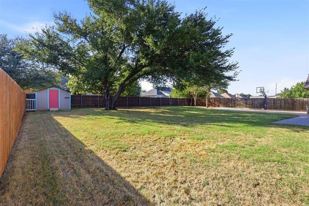 Spacious backyard with mature trees, privacy fencing, a storage shed, and a paved basketball court