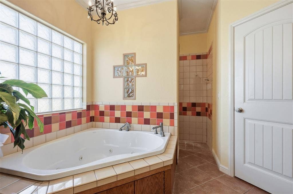 Built-in jetted tub with tile surround, glass block window, chandelier, walk-in shower with tile, and a paneled door