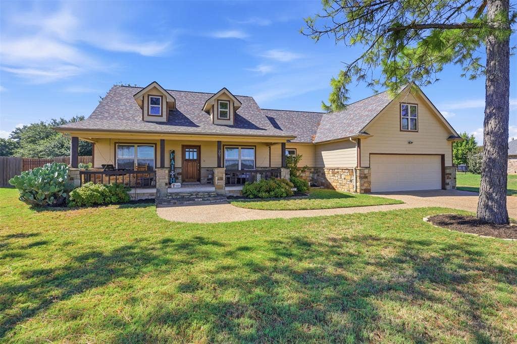 Exterior featuring a covered front porch, stone accents, dormer windows, an attached garage, and a concrete driveway