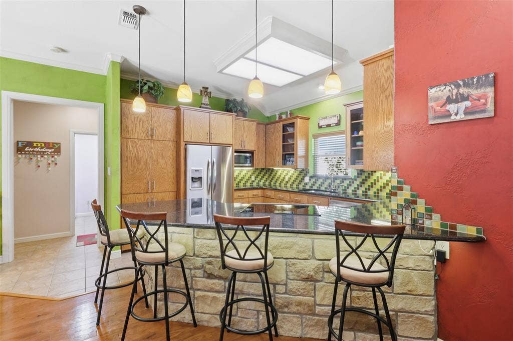 Kitchen featuring stone-clad breakfast bar, black granite countertops, wood cabinetry, stainless steel appliances, and a tiled backsplash