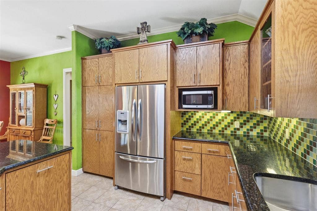 Stainless steel refrigerator with integrated dispenser, built-in microwave, wood cabinetry, dark countertops, and tile backsplash