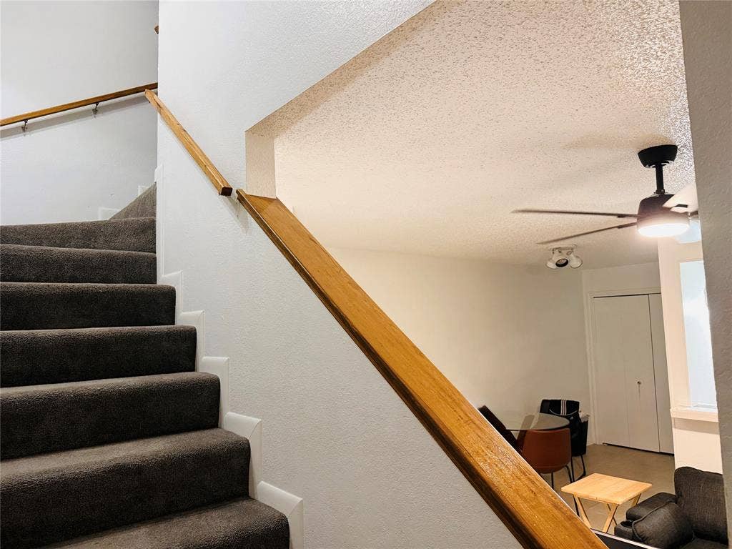 1915 S 10th Street, Waco, TX 76706 Carpeted staircase with wooden handrails, leading to a living area with a ceiling fan and track lighting