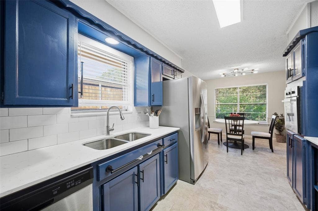 Kitchen featuring blue cabinetry, a stainless steel double basin sink, white subway tile backsplash, and a built-in oven