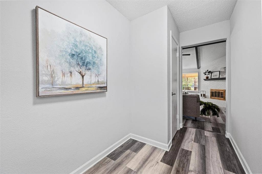 Wood-finish flooring with white trim, leading to an interior doorway with a black door handle, revealing a white brick fireplace with a wood mantel