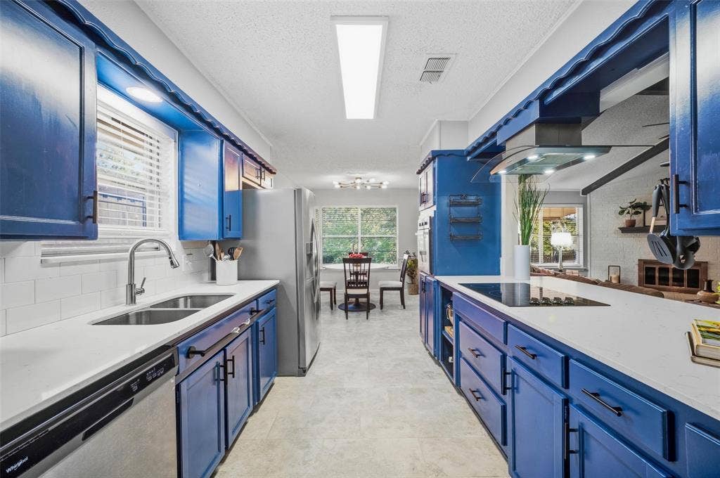 Galley kitchen featuring blue cabinetry, white countertops, stainless steel appliances, and a tiled backsplash