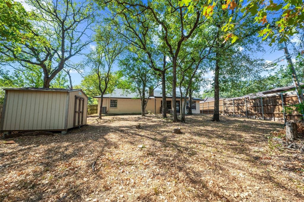 Expansive rear yard featuring mature trees, a detached storage shed, and perimeter fencing
