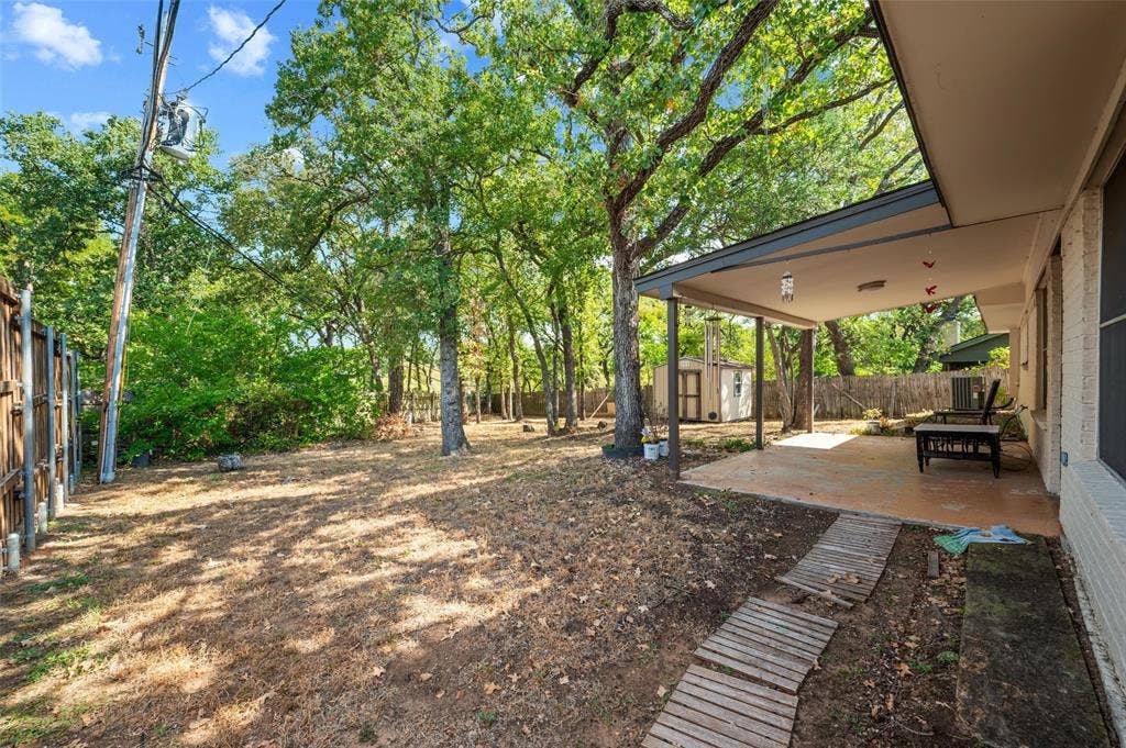 Expansive backyard with a covered patio, privacy fencing, mature trees, and a storage shed