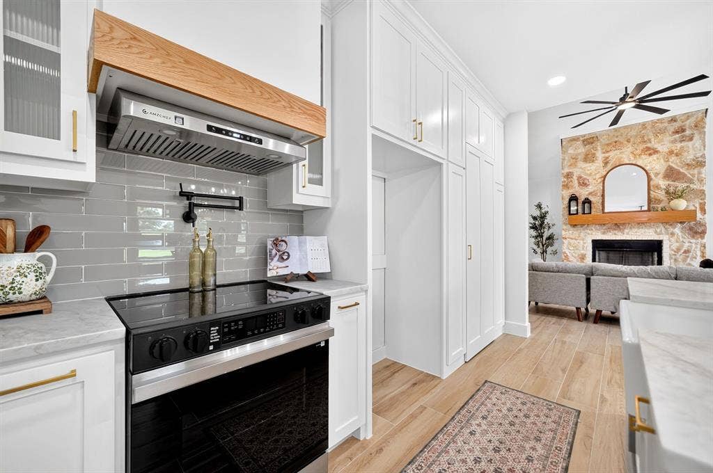 120 Springwood Road, Enchanted Oaks, TX 75156 Modern kitchen featuring a built-in oven, sleek range hood with wood trim, and subway tile backsplash