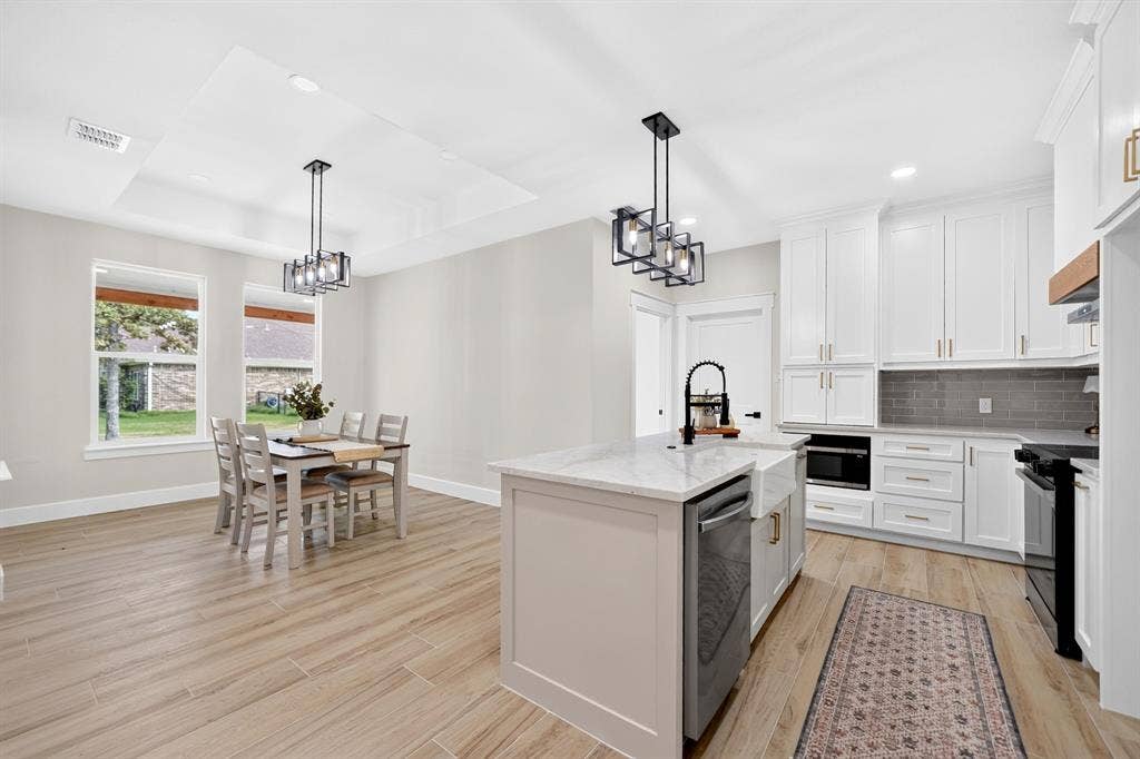 120 Springwood Road, Enchanted Oaks, TX 75156 Light wood-finish flooring throughout, white shaker-style cabinetry, kitchen island with a farmhouse sink, stainless steel appliances, and a tray ceiling