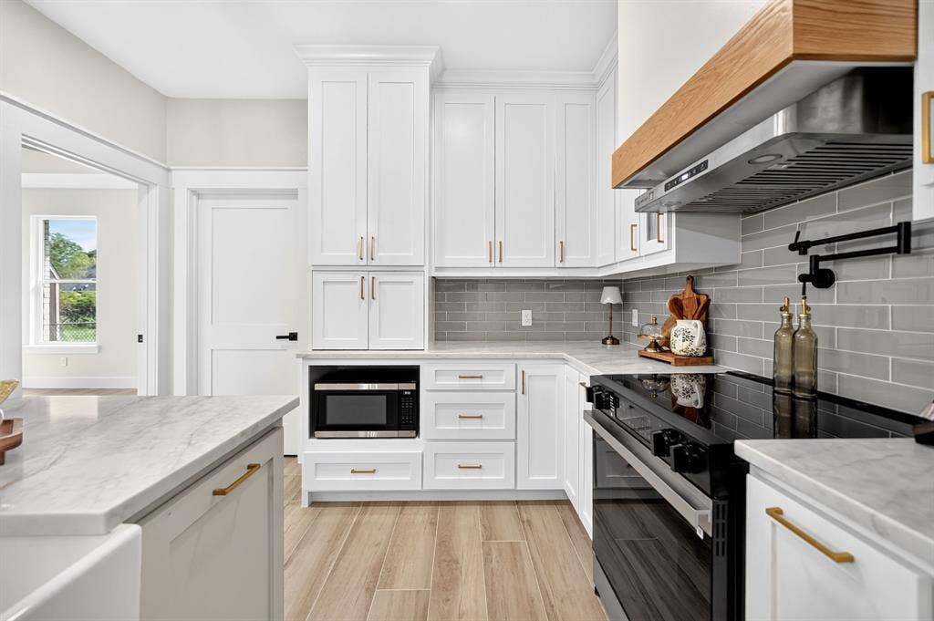 120 Springwood Road, Enchanted Oaks, TX 75156 White shaker cabinetry with gold-finish hardware, light-toned wood-finish flooring, white countertops, gray subway tile backsplash, and a wooden range hood