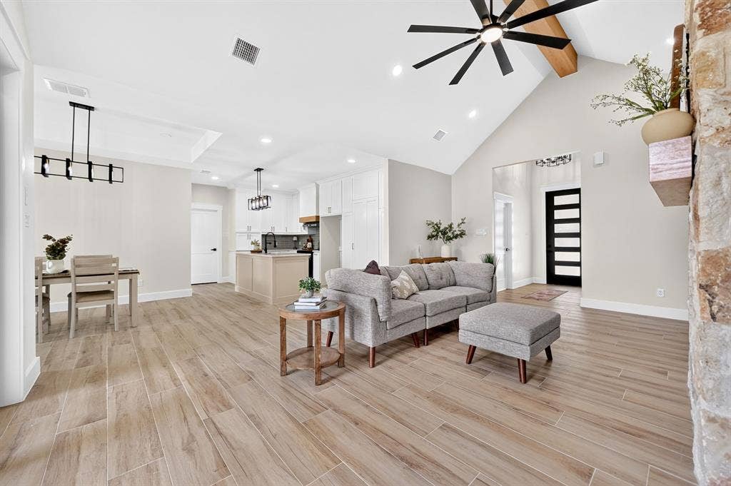 120 Springwood Road, Enchanted Oaks, TX 75156 Vaulted ceiling with exposed wood beam, wood-finish flooring, stone accent wall, tray ceiling, and a contemporary linear chandelier