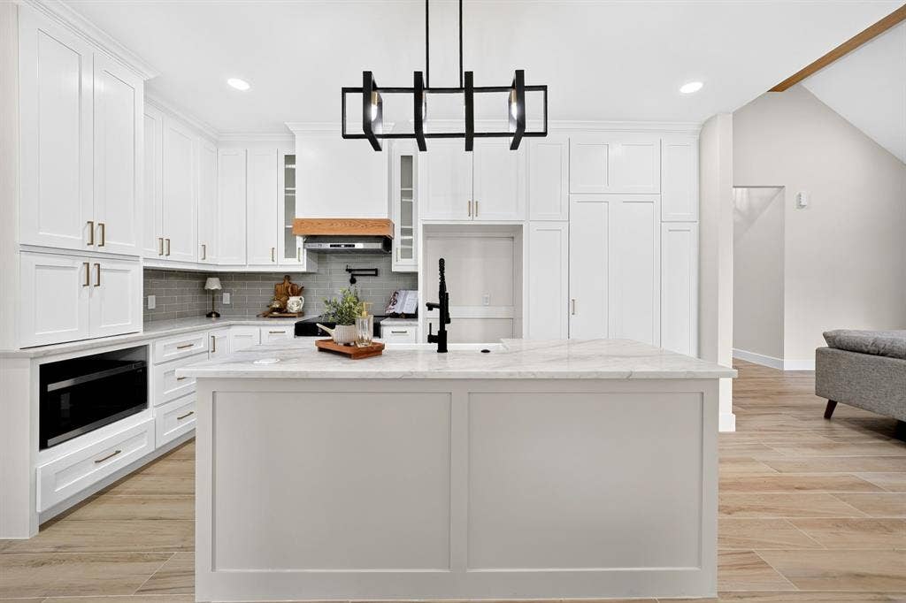 120 Springwood Road, Enchanted Oaks, TX 75156 White shaker cabinetry with gold-toned hardware, center island featuring a white stone countertop, wood-finish flooring, and a contemporary black chandelier