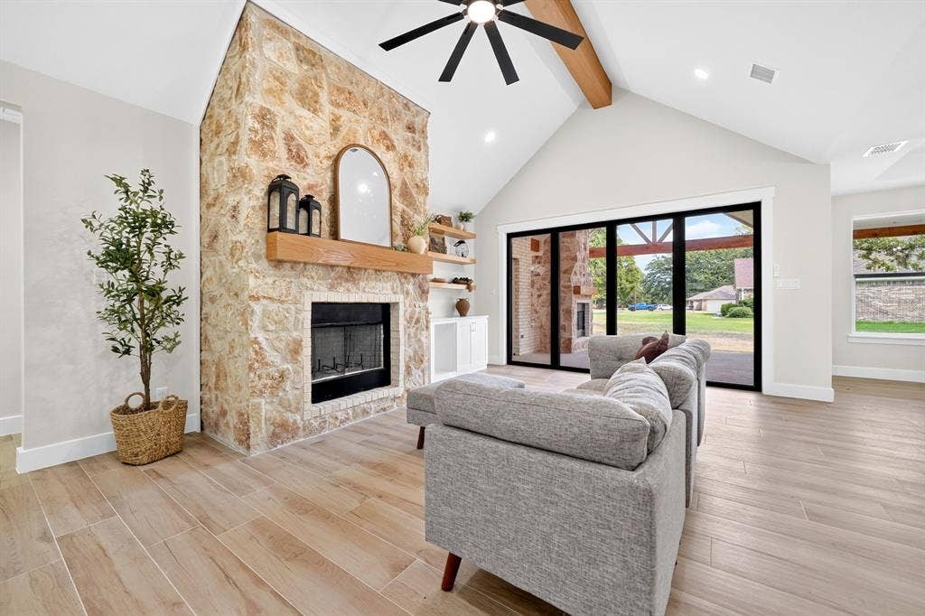 120 Springwood Road, Enchanted Oaks, TX 75156 Vaulted ceiling with exposed beam, stone-clad fireplace with wood mantel, wood-finish flooring, and large sliding glass doors