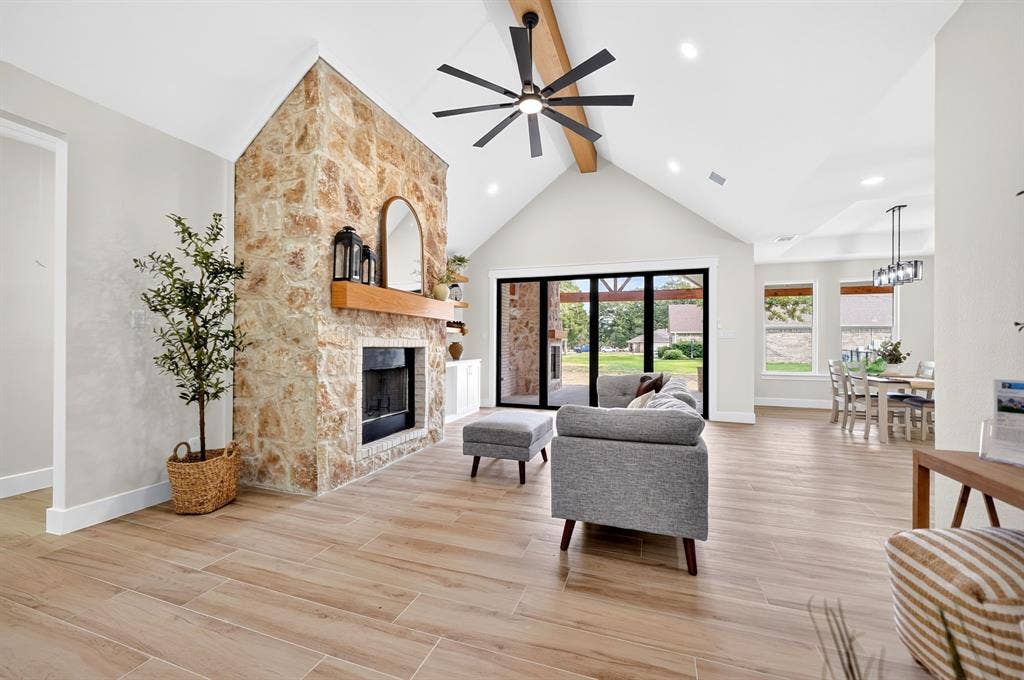 120 Springwood Road, Enchanted Oaks, TX 75156 Stone-clad fireplace with wood mantel, vaulted ceiling with exposed beam, wood-finish flooring, recessed lighting, and multi-panel sliding glass doors