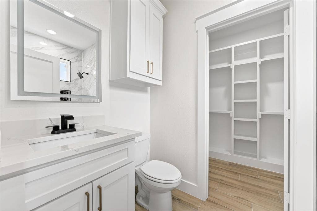 120 Springwood Road, Enchanted Oaks, TX 75156 Bathroom featuring a single vanity with a white countertop and integrated sink, a wall-mounted lighted mirror, a white toilet, and wood-finish flooring