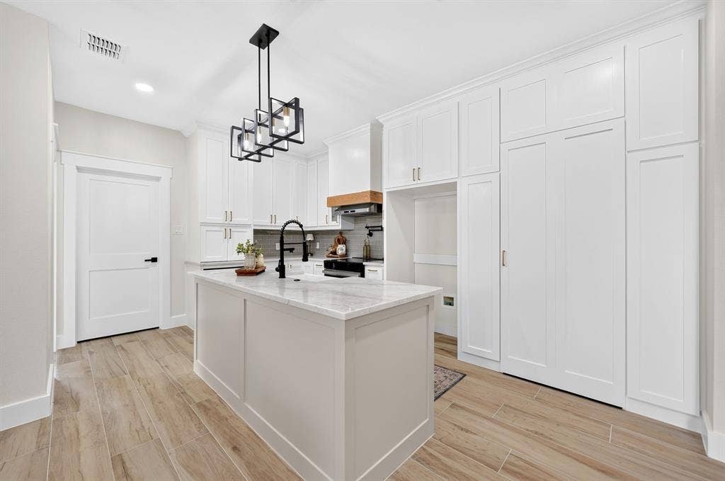 120 Springwood Road, Enchanted Oaks, TX 75156 Kitchen featuring an island with stone countertop, white cabinetry with crown molding, wood-finish flooring, and a modern light fixture