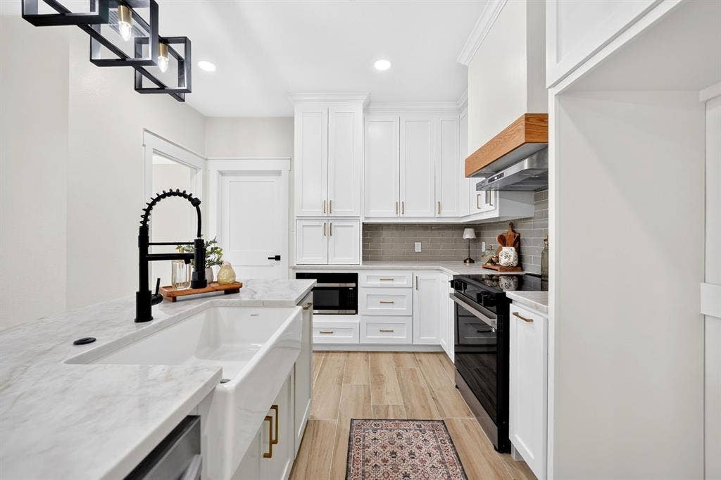 120 Springwood Road, Enchanted Oaks, TX 75156 White shaker cabinetry, light-toned wood-finish flooring, white farmhouse sink, black coil spring faucet, and a subway tile backsplash